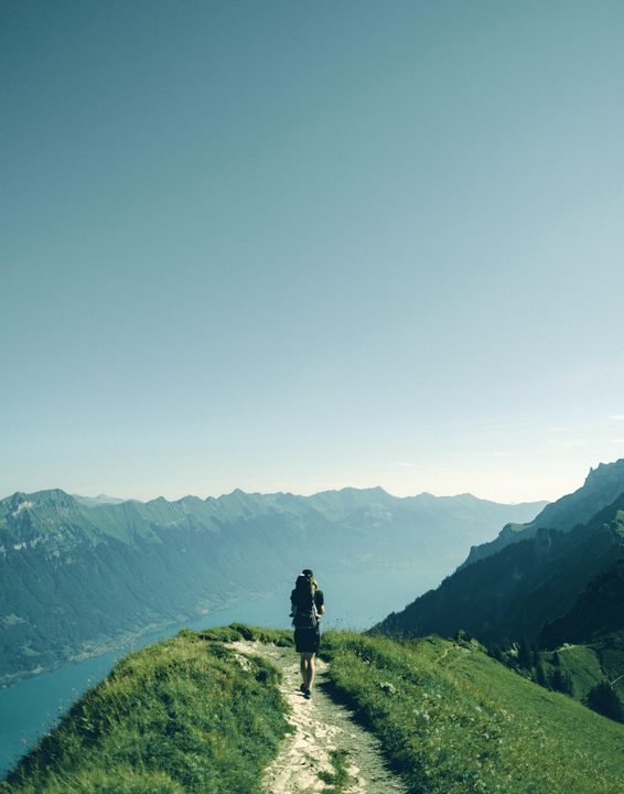 Hiker walking along a grassy mountain ridge above a lake