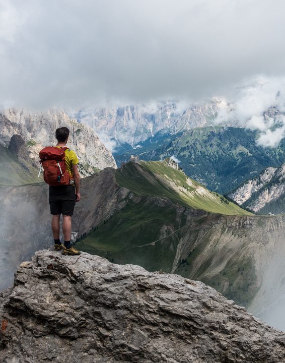 Hiker with a red backpack standing on a rock above a mountain valley