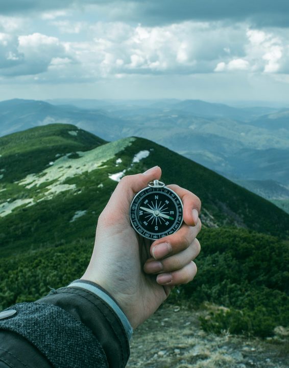 Hand holding a compass against green mountain slopes